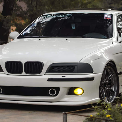 A BMW E39 5 Series cruising along a scenic coastal road, capturing the vehicle's dynamic stance and the driving pleasure it offers, embodying the essence of BMW's "Ultimate Driving Machine" slogan.

