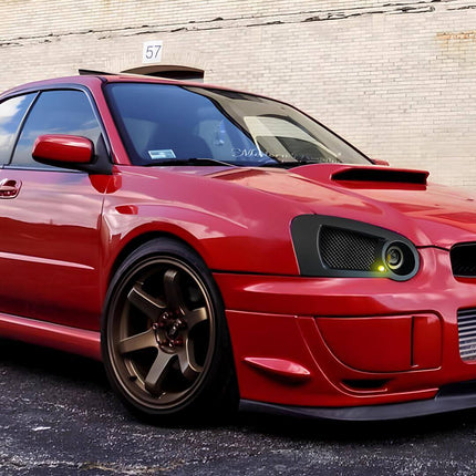 Interior shot of a 2005 Subaru Impreza WRX, featuring black cloth seats with red stitching, a leather-wrapped Momo steering wheel, and a factory-installed boost gauge, illustrating the driver-centric cabin design.

